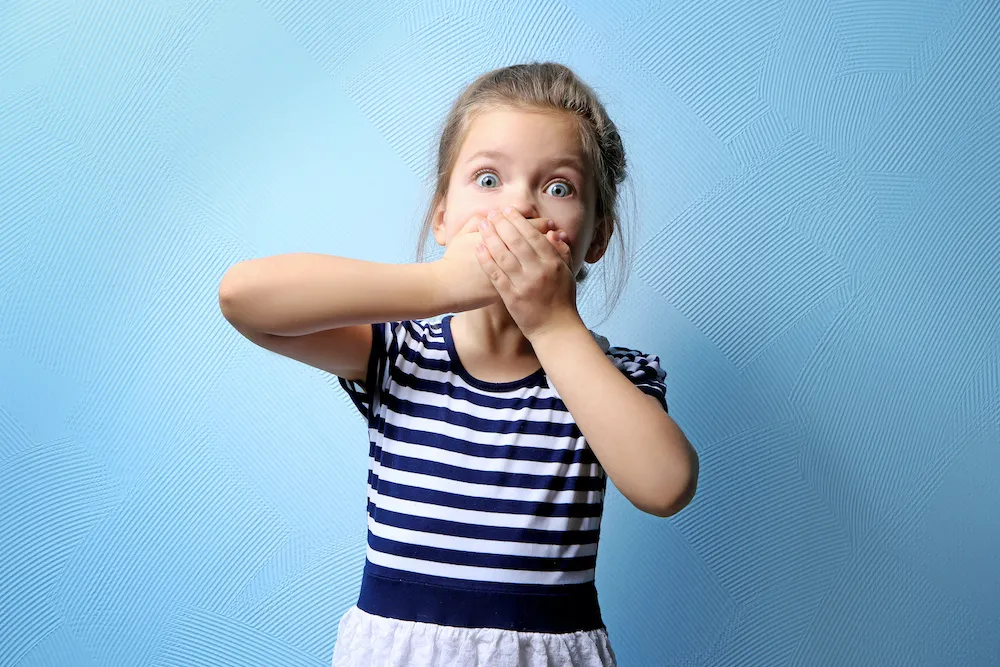 Cute little girl covering mouth with hands, on color background