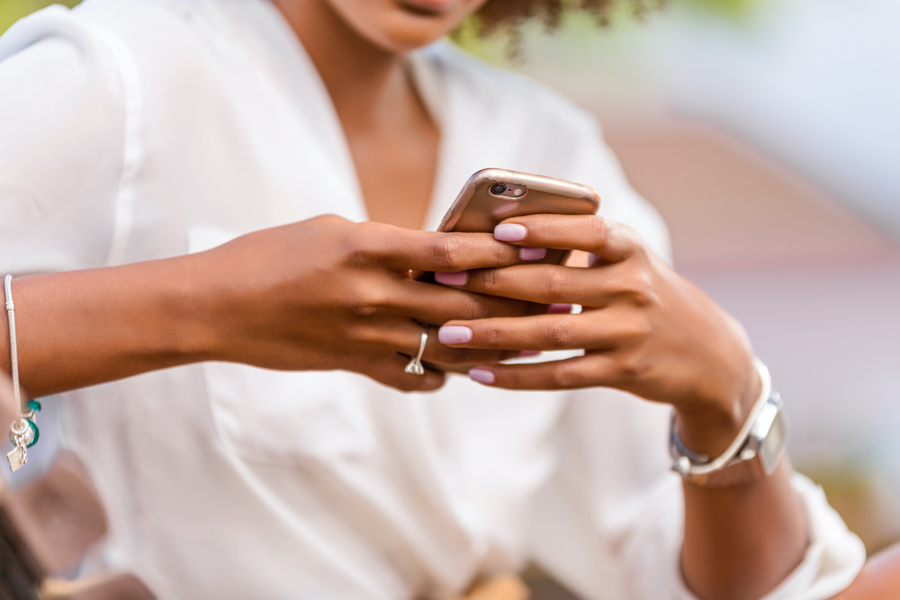 Outdoor portrait of a Young black African American young woman texting on mobile phone