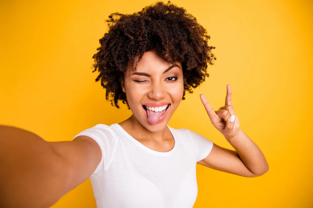 Close up photo beautiful amazing she her dark skin lady hand rock fan concert music lover tongue out mouth video translation wear casual white t-shirt isolated yellow bright vibrant vivid background