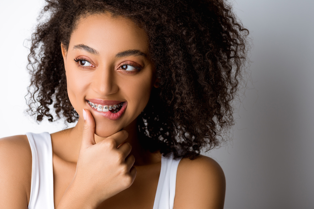 thoughtful smiling african american girl with dental braces touching lip, isolated on grey